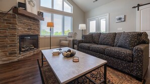 A living room with a fireplace, a sofa, a coffee table, and a large window. - New Build 3BR Branson Condo w/ Arcade + Indoor Pool | FH G-303 (Branson)