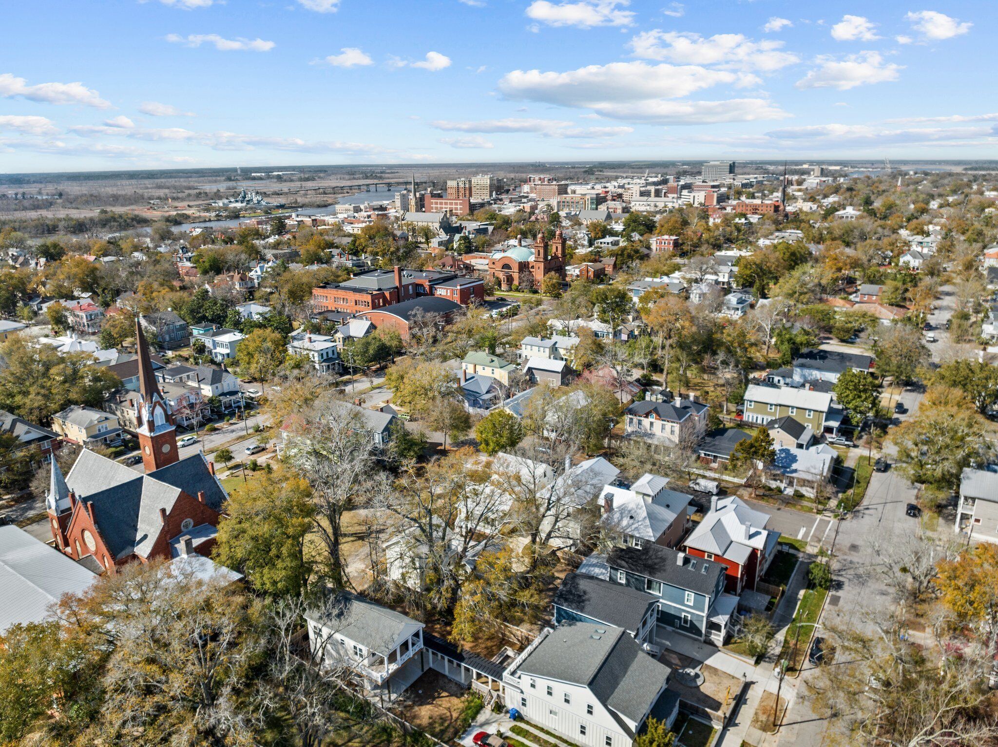 Vista aérea de un pueblo con diversos edificios, entre ellos una iglesia destacada con campanario, casas residenciales y una combinación de estructuras comerciales.