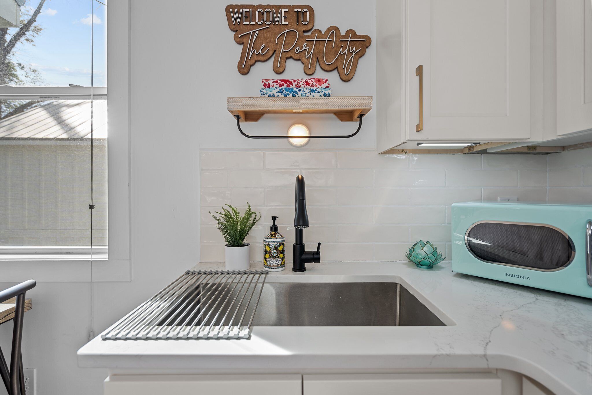 A kitchen with a stainless steel sink, a black faucet, a teal-colored microwave, and a decorative sign above the sink.