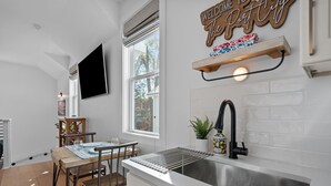 A modern kitchen with a built-in sink, a dining area with a table and chairs, a large window, and a wall-mounted TV. - The Yak Shack: Carriage House in Historic District - 4 blocks from Riverwalk (Wilmington)