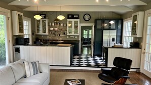 Una cocina moderna con armarios blancos, piso a cuadros blanco y negro, y un comedor con una silla de cuero negro y un sofá blanco.