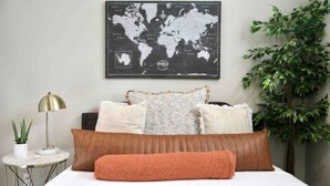 A neatly made bed with a world map above it, a small side table with a lamp, and a potted plant to the right. - Bright and Charming Guest House (10 mins from LAX) (Los Angeles)