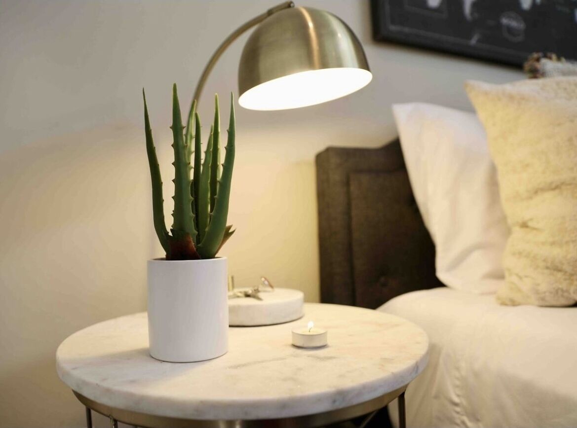 A round marble table with a white pot containing a succulent plant, a small white candle, and a modern floor lamp.