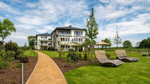 A modern building with a pathway leading to a grassy area with lounge chairs and umbrellas. - Haffhaus 1 - Haffhaus (Garz)
