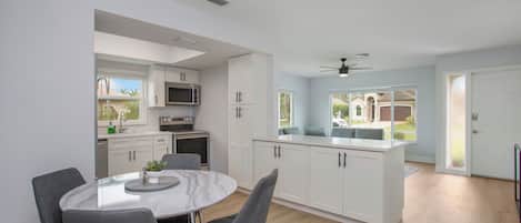 A modern kitchen with white cabinets, a central island, and a dining area with a round table and chairs.