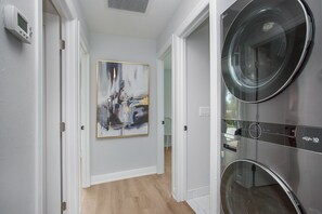 A hallway with a modern art piece, a washing machine, and a thermostat on the wall. - Heated Pool & Spa – Near the Beach, Bikes Included (Naples)