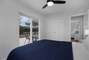 A bedroom with a bed, a ceiling fan, a sliding glass door leading to an outdoor patio with a table and chairs, and a white wardrobe. - Heated Pool & Spa – Near the Beach, Bikes Included (Naples)