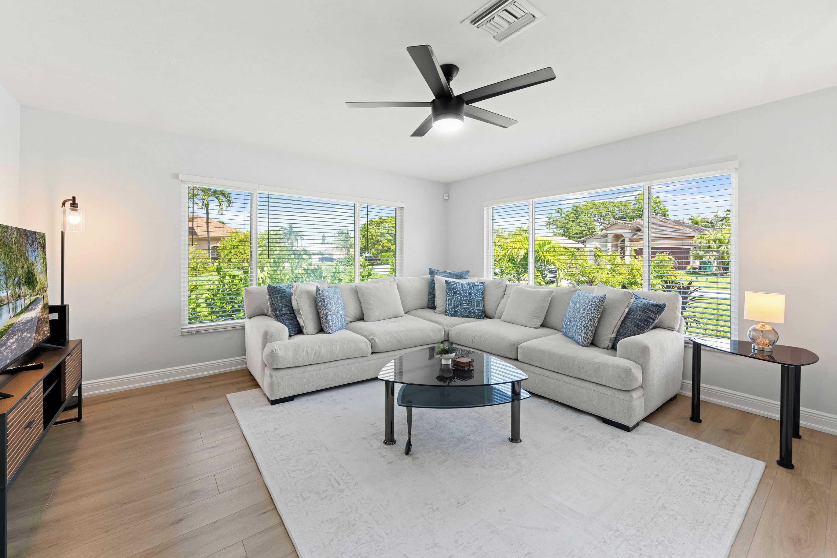 A modern living room with a sectional sofa, a glass coffee table, and a ceiling fan.