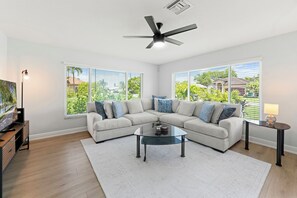 A modern living room with a sectional sofa, a glass coffee table, and a ceiling fan. - Heated Pool & Spa – Near the Beach, Bikes Included (Naples)