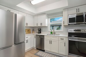 A modern kitchen with white cabinets, stainless steel appliances, and a window providing natural light. - Heated Pool & Spa – Near the Beach, Bikes Included (Naples)