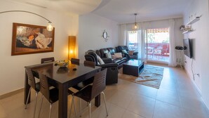 Ein modernes Wohnzimmer mit Essbereich, ausgestattet mit einer Sofagarnitur, einem Esstisch mit Stühlen, einem Couchtisch und einem Bild an der Wand.
