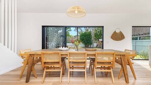 Comedor con mesa y sillas de madera, lámpara colgante y vista al exterior por un ventanal.