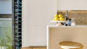 Una cocina con cubierta blanca, un taburete de madera y un vaso de agua.