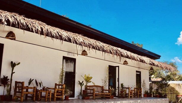 A building with a thatched roof and a tiled porch with wooden furniture. - Hangover Hostel (Moalboal)