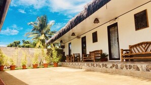 A building with a thatched roof, potted plants, and wooden furniture on the porch. - Hangover Hostel (Moalboal)