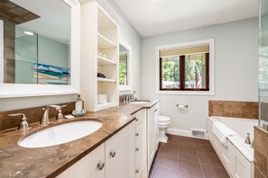 Ein modernes Badezimmer mit zwei Waschbecken, einer Toilette und einer Badewanne. Ein Fenster bietet Blick auf Grünflächen.