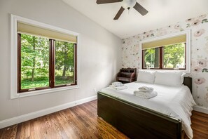 Un dormitorio con un ventanal grande, una cama, una mesita de noche y un ventilador de techo.