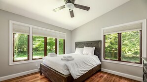 Un dormitorio con cama de madera, ventanas amplias y ventilador de techo.