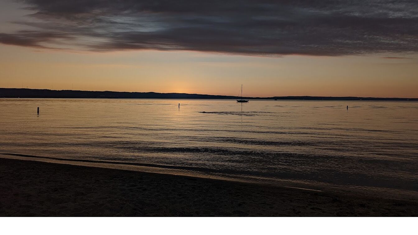 Une plage aux eaux calmes, avec un voilier à l’horizon.