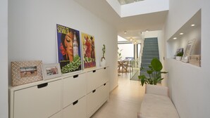 Um interior moderno com um console branco exibindo obras de arte e um sofá. Uma escadaria leva a um andar superior.