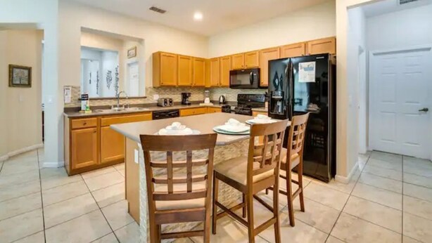 A modern kitchen with wooden cabinets, a central island, and a black refrigerator.