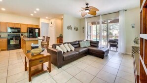 A spacious living area with a brown leather sofa, a wooden coffee table, and a kitchen in the background.