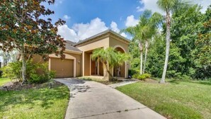 A residential house with a driveway, a lawn, and palm trees.