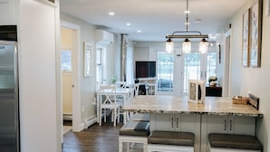 Una cocina moderna con armarios blancos, una isla central con taburetes y un refrigerador de acero inoxidable.