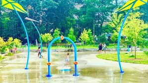 Ein Wasserpark mit blauen Bögen und gelben Fahnen, der Wasserspielbereiche und einen gepflasterten Weg zeigt.