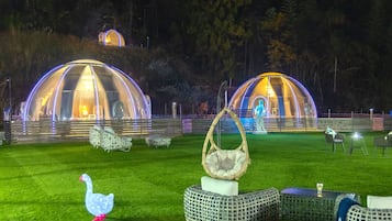 Uma área externa bem iluminada com estruturas em cúpula transparente, móveis de vime e uma figura decorativa de ganso.