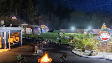 Espaço ao ar livre à noite com lareira, assentos e uma tenda.