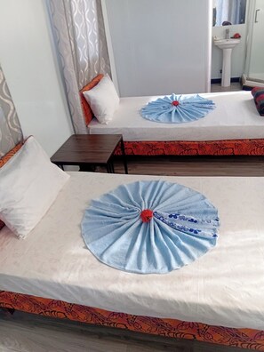 A hotel room with two beds, each with a neatly folded blue towel and a red flower centerpiece. There is a small wooden table and a white sink in the corner. - Shalini Garden Hotel & Apartment (Sigatoka)