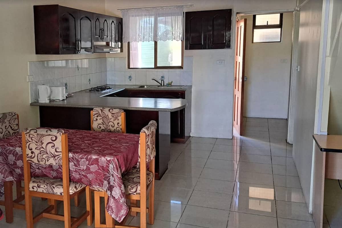 A compact kitchen with a dining area, featuring a small island, dark cabinets, and a window with a white curtain.