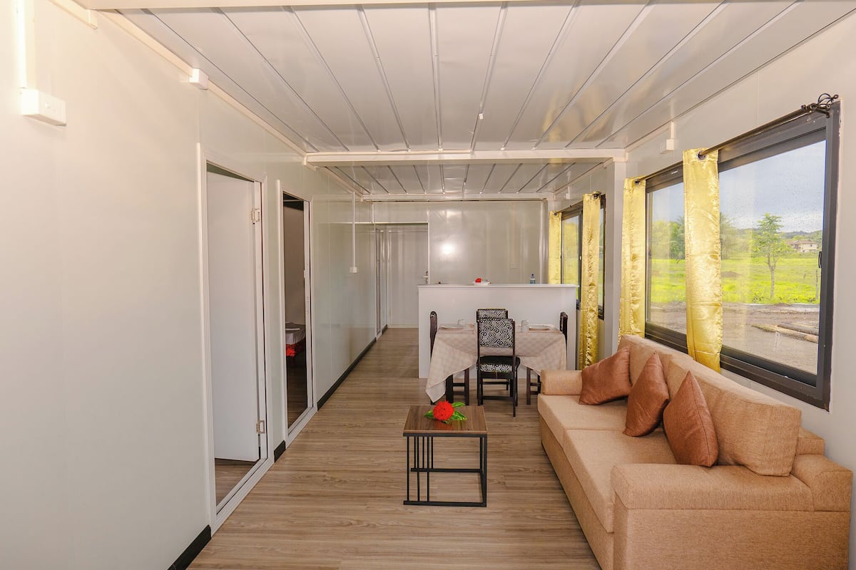A corridor with a sofa, a table with a flower, and a dining area with chairs and a table.