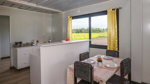 Une cuisine compacte avec un coin repas, comprenant une fenêtre avec des rideaux, un petit îlot et une table dressée pour deux personnes.