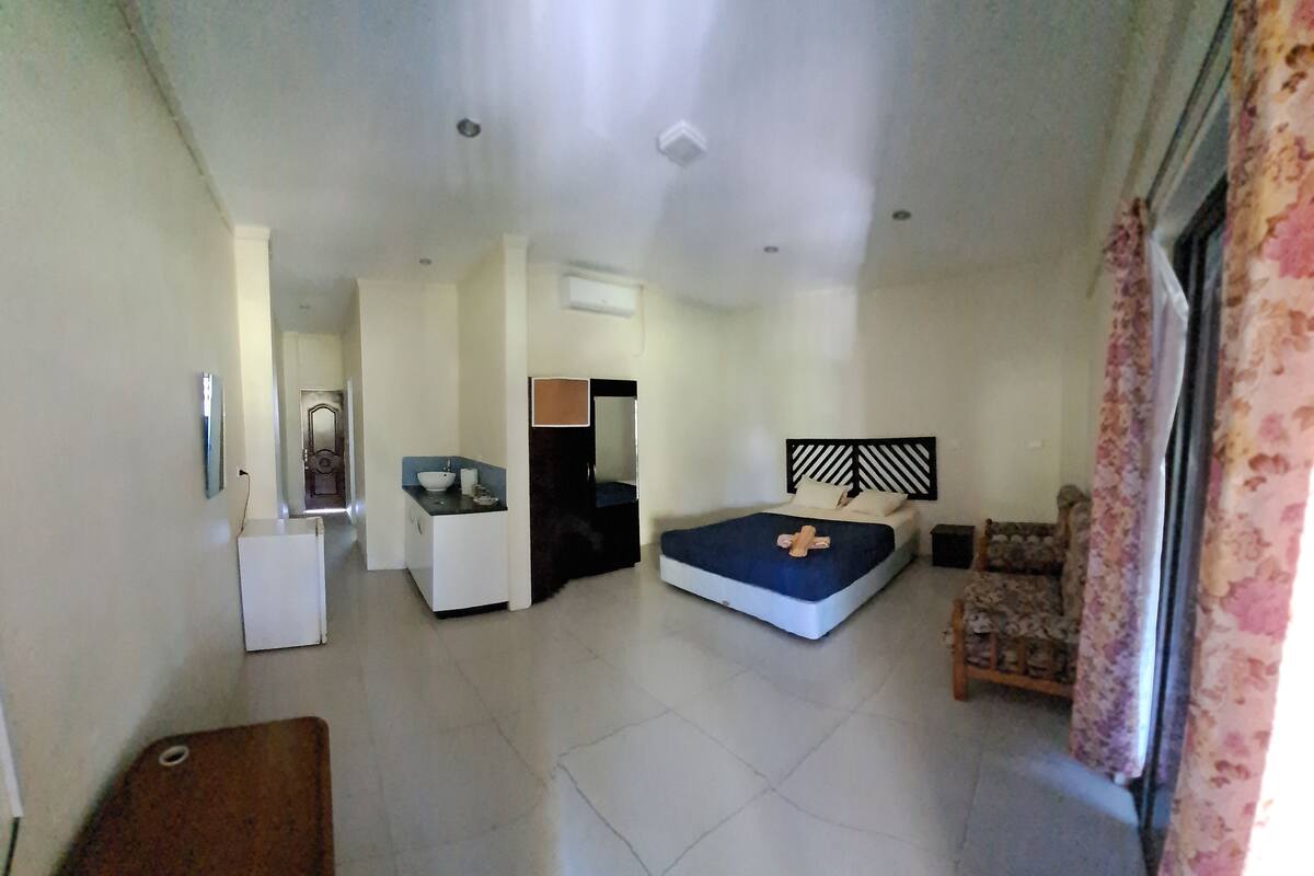 A modern, well-lit room with a bed, a small desk, a chair, and a bathroom.