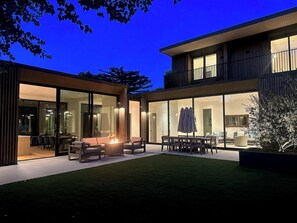 Et moderne hus med to etager og en patio med bålsted og udendørs møbler.