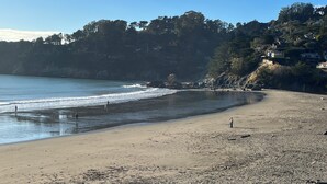 Una playa con costa rocosa, agua tranquila y un cerro boscoso al fondo.