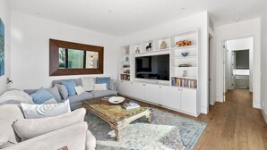 Un salón amplio con una televisión grande, armarios blancos y una zona de estar acogedora.