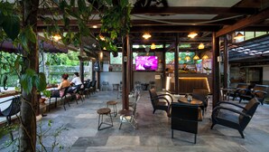 Un café al aire libre con suelo de piedra, mesas y sillas de madera y plantas colgantes.