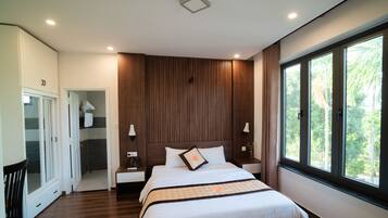 A modern bedroom with a large bed, wooden panel wall, and a window with a view of greenery.