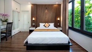 Un dormitorio moderno con una cama grande, mesitas de noche, un escritorio y vistas a zonas verdes a través de la ventana.