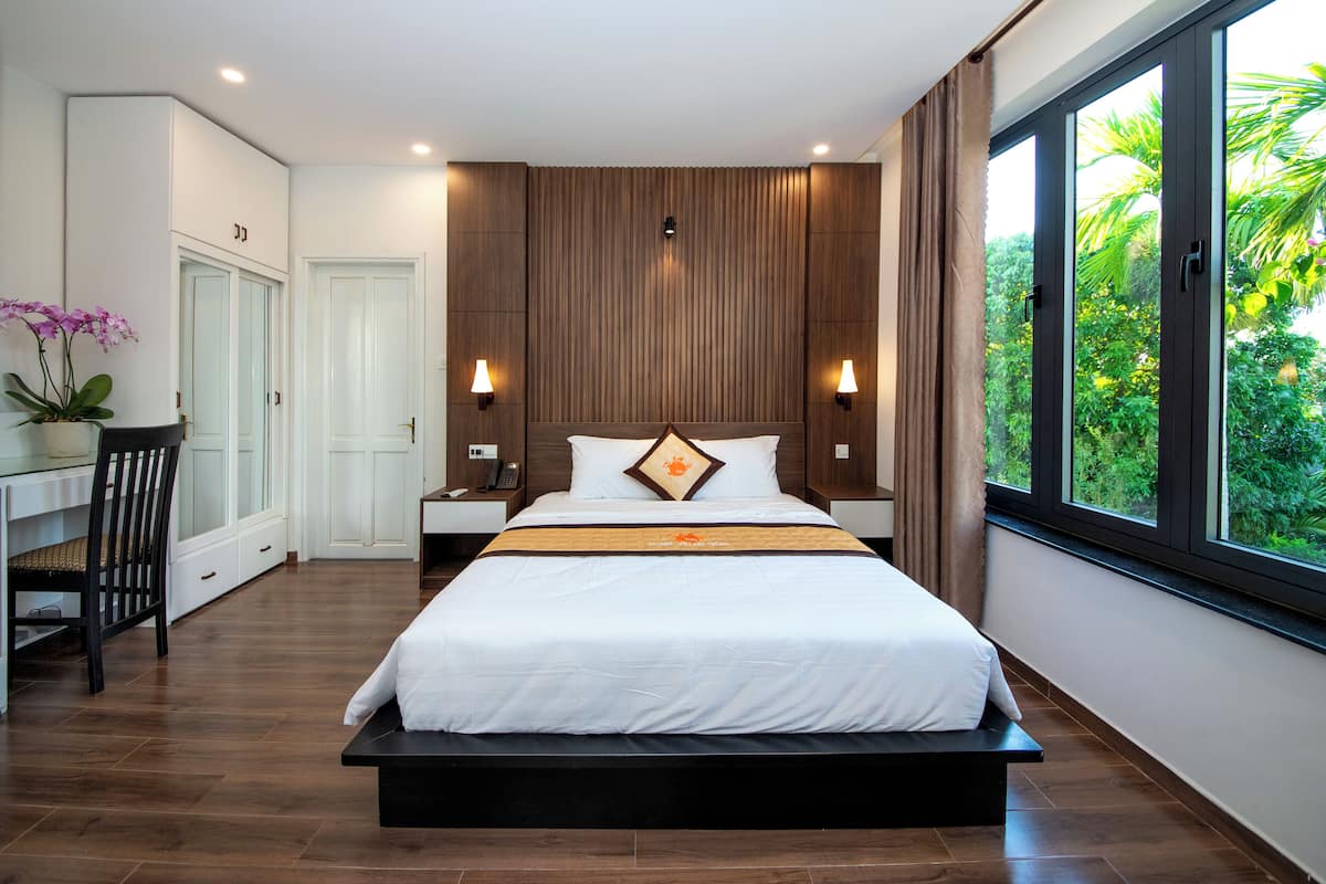 A modern bedroom with a large bed, bedside tables, a desk, and a view of greenery through the window.