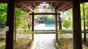 Un espacio al aire libre cubierto con piscina, rodeado de follaje y una estructura de madera.