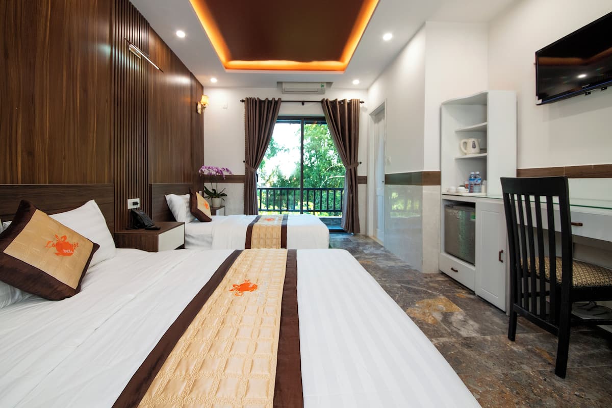 A hotel room with two beds, a desk, a chair, a TV, and a balcony with a view of greenery.