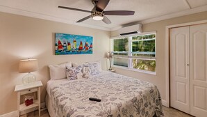 Ein Schlafzimmer mit einem Bett, Deckenventilator, einem Gemälde, einem Fenster mit Jalousien und einer Tür.