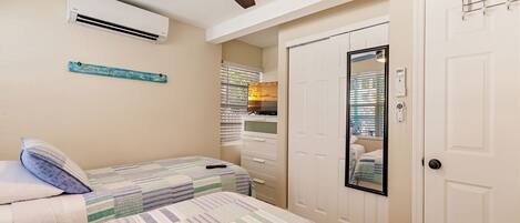 Quarto com duas camas, um ventilador de teto, um aparelho de ar condicionado, um espelho e uma porta branca.