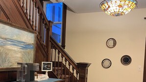 A staircase with wooden railings, a coffee machine, a framed painting, and a stained glass ceiling light fixture.