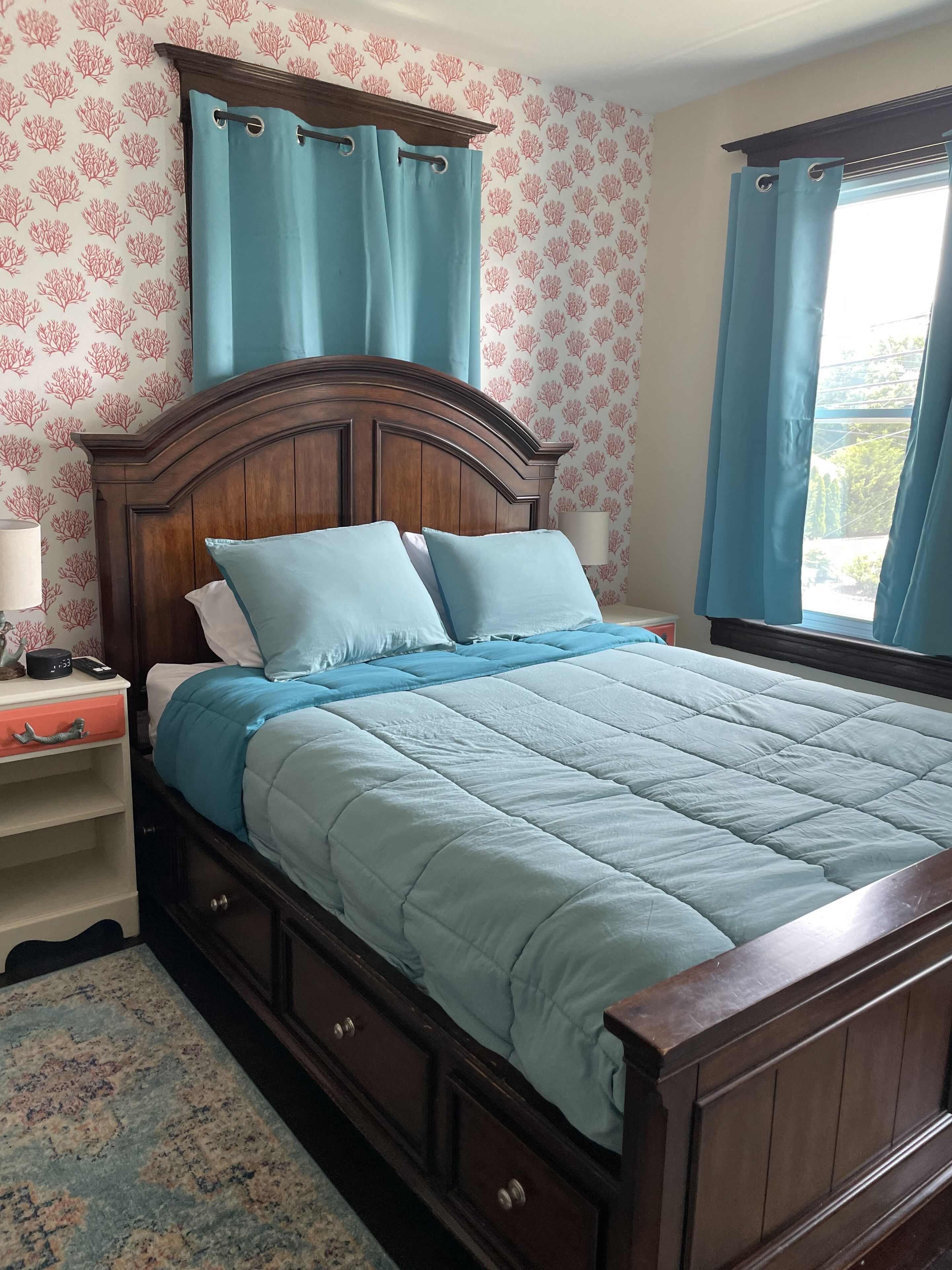 A bedroom with a wooden bed, a nightstand, a lamp, and a window with curtains.