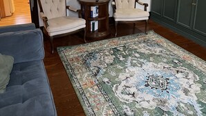 A living room with a blue sofa, two armchairs, a round wooden table, a patterned rug, and a green cabinet with a small sign.